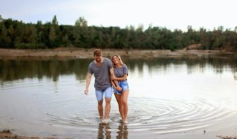 couple wearing grey t shirts walking on shallow water and smiling