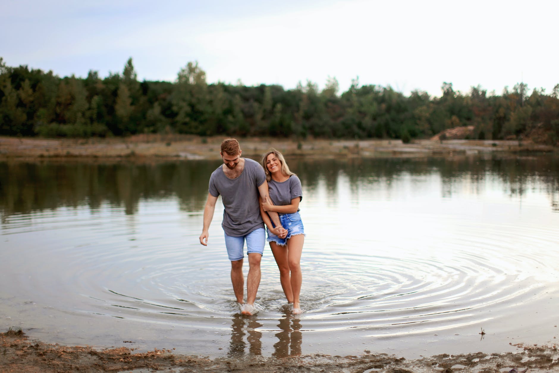 couple wearing grey t shirts walking on shallow water and smiling