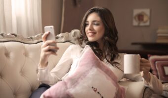 woman in white long sleeved shirt holding smartphone sitting on tufted sofa